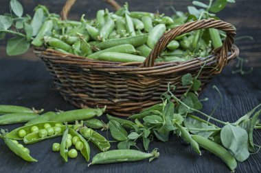 Saman sepetinde taze yeşil bezelye. Koyu ahşap arka plan.