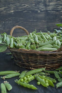 Saman sepetinde taze yeşil bezelye. Koyu ahşap arka plan.