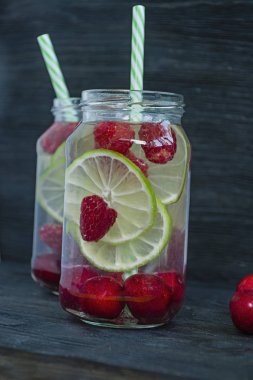 Meyve ile ferahlatıcı yaz içeceği. Kiraz, ahududu, limondan yapılmış içecek. Koyu ahşap arka plan.