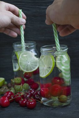 Meyve ile ferahlatıcı yaz içeceği. Kiraz, bektaşi üzümü, limondan yapılmış içecek. Koyu ahşap arka plan.