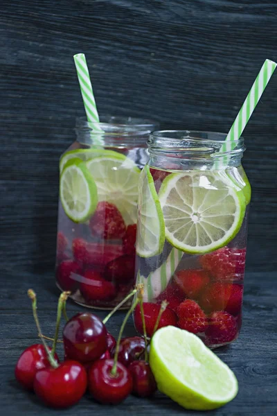 Meyve ile ferahlatıcı yaz içeceği. Kiraz, ahududu, limondan yapılmış içecek. Koyu ahşap arka plan.