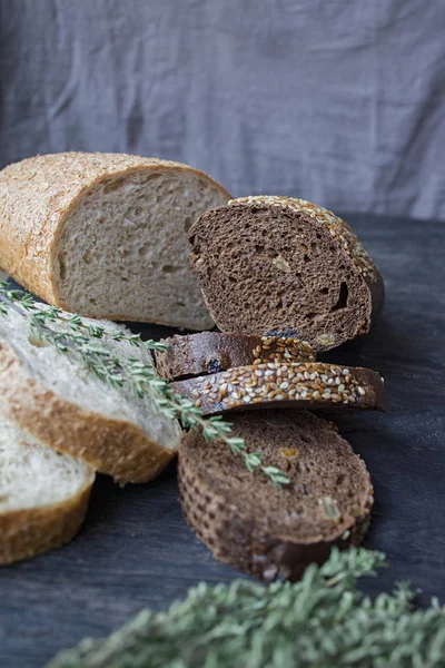 Loaves of black and white bread on a black board background. Still life, captured from the side. — Stock Photo, Image