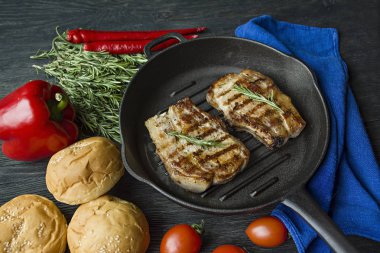 Siyah ahşap arka planda et, biberiye, yeşillikler ve sebzeler için baharatlar ile süslenmiş yuvarlak ızgara tavada ızgara biftek.