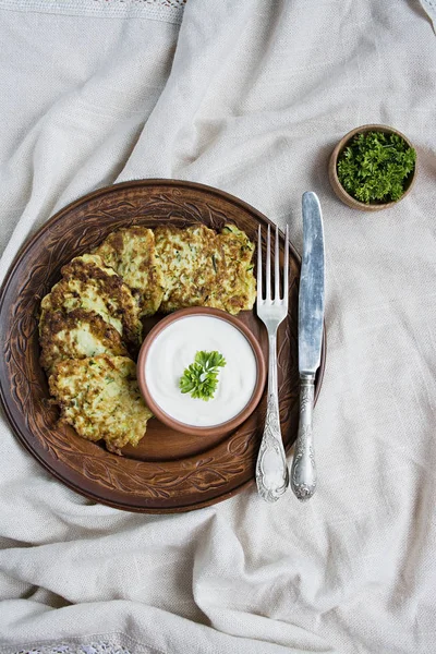 Zucchini fritters, vegetarian zucchini pancakes, served with fresh herbs and sour cream, top view. Light background. — Stock Photo, Image