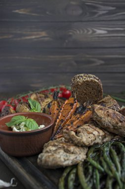 Izgara sebzeler ve tavuk fileto bir kesme tahtasında servis edilir. Koyu ahşap arka plan.