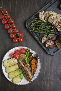 Kiraz domates, yeşillikler, biber rulo ile farklı varyasyonlarda kızarmış tavuk göğsü. Ahşap arka plan.