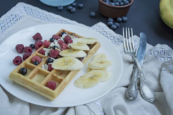 Waffles with fresh banana, raspberries, blueberries for breakfast. Belgian waffles. Dark wooden background.