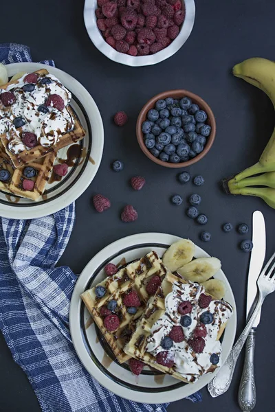 Waffles with fresh banana, raspberries, blueberries for breakfast. Belgian waffles. Dark wooden background.