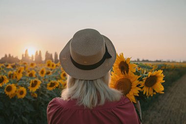 Gün batımında ayçiçeği içindeki kız. Bir buket ayçiçeği ile bir şapka ve yaz elbise kız.