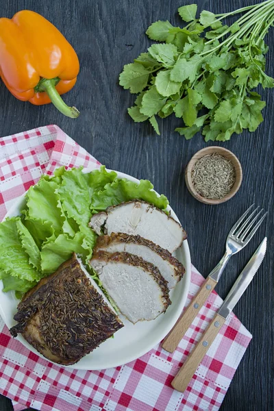 Baked pork tenderloin in spices sliced on a white plate with green salad. Dark wooden background.