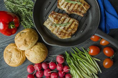 Siyah ahşap arka planda et, biberiye, yeşillikler ve sebzeler için baharatlar ile süslenmiş yuvarlak ızgara tavada ızgara biftek.