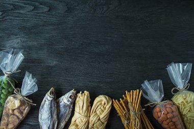 Bira, fındık ve kraker için atıştırmalıklar. Bira atıştırmalıkları selofan içinde paketlenir. Koyu ahşap arka plan. Metin için alan.