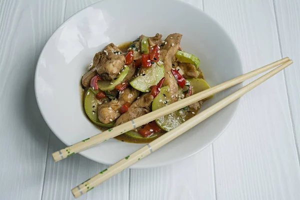 Salada quente com frango, abobrinha e pimenta, polvilhada com sementes de gergelim e ervas. Comida asiática. Fundo de madeira branca . — Fotografia de Stock