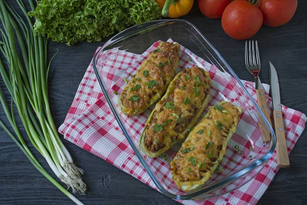 Zucchine ripiene con carne macinata e formaggio grattugiato in una teglia di vetro. Sfondo in legno scuro . — Foto Stock