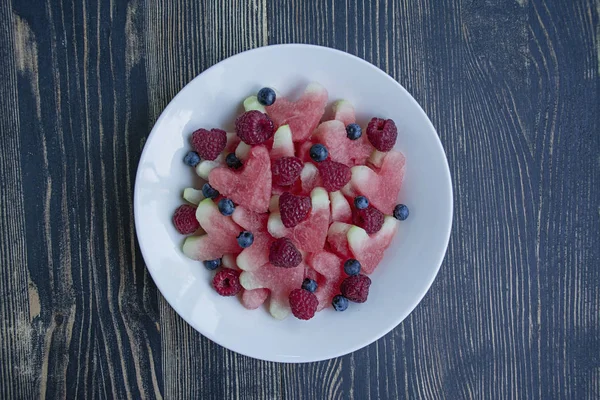 Kalp ler şeklinde karpuz, ahududu, beyaz tabakta yaban mersini. Metin için boşluk. Meyveli atıştırmalık. Sevgililer günü için aşk konsepti.