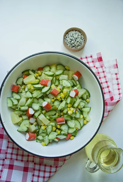 Salat mit Mais, Krabbenstangen, Gurken in einer weißen Schüssel auf weißem Hintergrund. vegetarischer Salat. Kochprozess. — Stockfoto