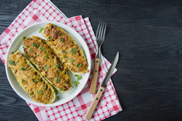 Zucchine ripiene con carne macinata e formaggio grattugiato in una teglia di vetro. Sfondo in legno scuro . — Foto Stock