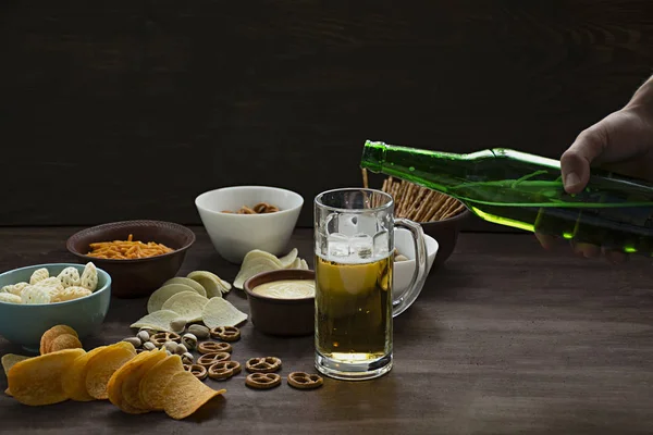 Male hand pours beer. Beer with pretzels and various snacks. Beer snacks. Wood background. View from above. Place for text.