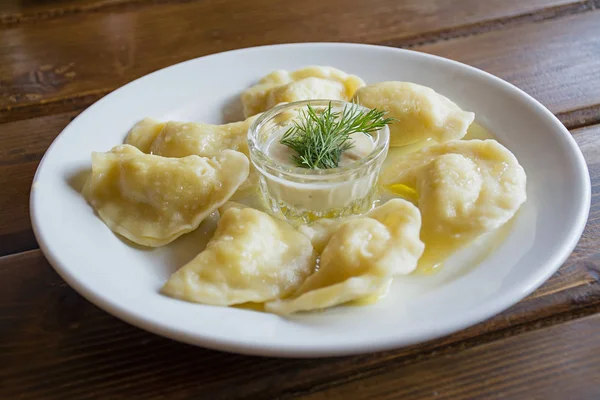 Dumplings op een witte plaat met zure room. -Traditioneel Oekraïens eten. — Stockfoto