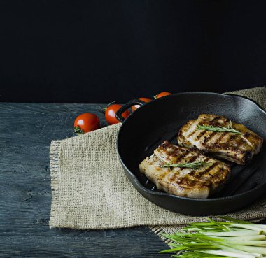 Yuvarlak bir ızgara tavada ızgara biftek, et, biberiye, yeşillik ve koyu ahşap arka plan üzerinde sebze için baharat ile süslenmiş. Metin için yer.