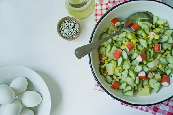 Salat mit Mais, Krabbenstangen, Gurken in einer weißen Schüssel auf weißem Hintergrund. vegetarischer Salat. Kochprozess. — Stockfoto
