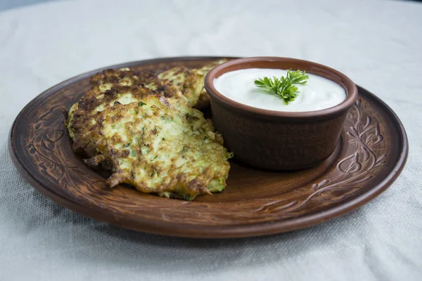 Frittelle di zucchine, frittelle di zucchine vegetariane, servite con erbe fresche e panna acida, vista dall'alto. Sfondo chiaro . — Foto Stock