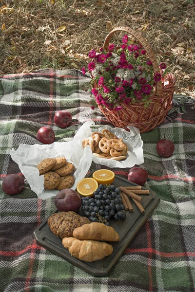 Autumn picnic in the park. Basket with flowers on a blanket. Tea, croissants, cookies, grapes in yellow autumn leaves. Autumn concept.