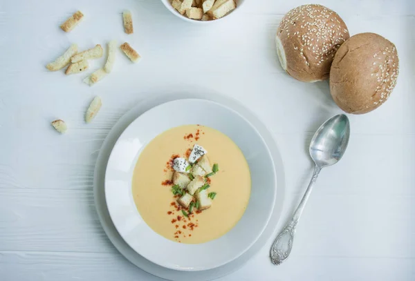 Сырный суп с крекерами, травами и сыром фета. Суп со сливками подается в белой тарелке. Белый фон . — стоковое фото