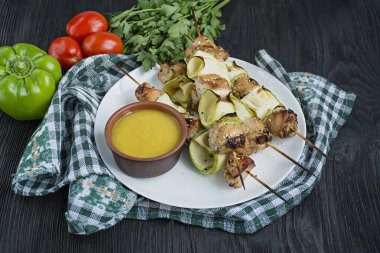 Beyaz bir tabak tabaktabaktabaktabaktabaktabaktabaktabaktabaktabaktabaktabaktabaktabaktabaktabaktabakta kabak, sebze ve otlarla şişler. Koyu ahşap arka plan.