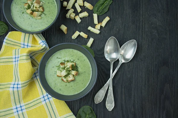 Creamy spinach soup with crackers, herbs and chia seeds. Green soup served in a bowl on a wooden table. Space for text. Flat lay.