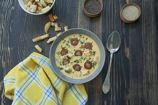 Сырный суп с жареными сосисками и травами. Суп со сливками подается в тарелке. Темный деревянный фон . — стоковое фото