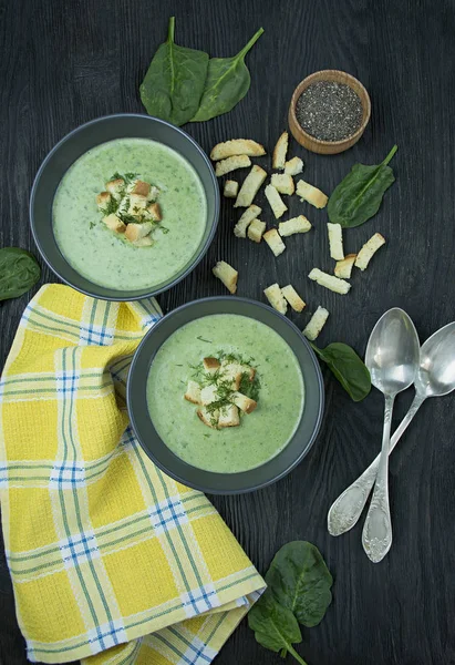 Creamy spinach soup with crackers, herbs and chia seeds. Green soup served in a bowl on a wooden table. Flat lay.