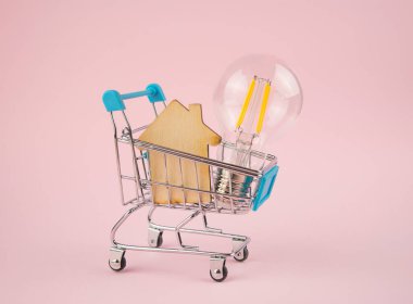 İş konsepti. Pembe arka planda, alışveriş arabasında ahşap bir evi olan lamba. Bir ev alıyorum. İş fikirleri, beyin fırtınası. Boşluğu kopyala