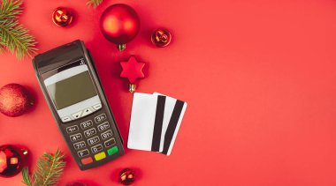 Noel alışverişi. Kırmızı arka planda Noel dekoru olan banka kartlı bir terminal. Baner. Boşluğu kopyala.