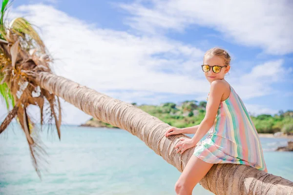 Entzückendes kleines Mädchen sitzt während der Sommerferien auf einer Palme am weißen Strand — Stockfoto