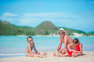 Tropikal beyaz Beach aile yapma Kumdan kale. Baba ve iki kız tropik sahilde kum ile oynamak