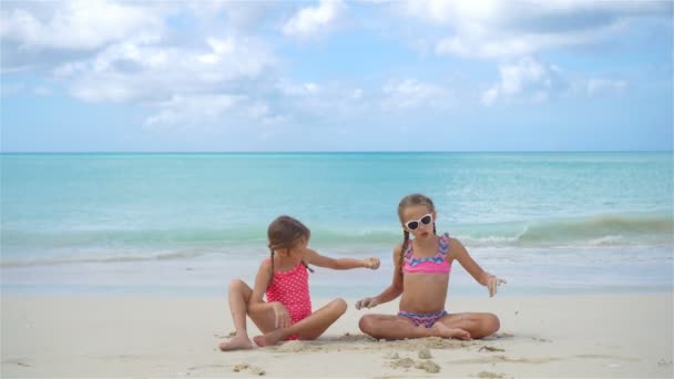 Две маленькие счастливые девочки веселятся на пляже, играя вместе с песком — стоковое видео