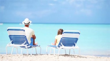 Baba ve kızı plajda şezlong üzerinde oturan