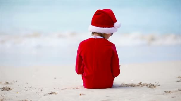 Маленькая девочка в рождественской шляпе на белом пляже во время рождественских каникул — стоковое видео