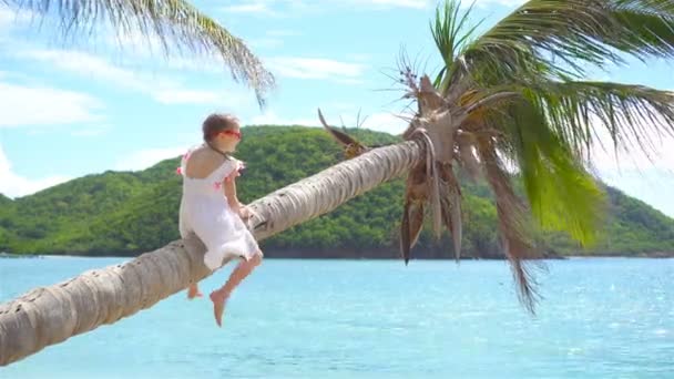Adorable little girl at tropical beach sitting on palm tree during summer vacation — Stock Video