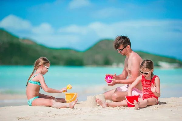 Father and two girls playing with sand on tropical beach — Stock Photo, Image