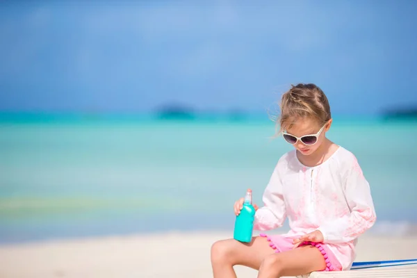 Niña con botella de crema solar sentada en la playa tropical —  Fotos de Stock