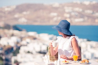 Mikonos kentine muhteşem manzaralı açık kafede kahvaltı güzel zarif kız. Resort Restoran deniz manzaralı lüks otel terasında sıcak kahve içme kadın.