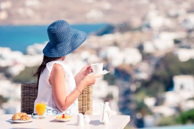 Mikonos kentine muhteşem manzaralı açık kafede kahvaltı yapıyor kadın.
