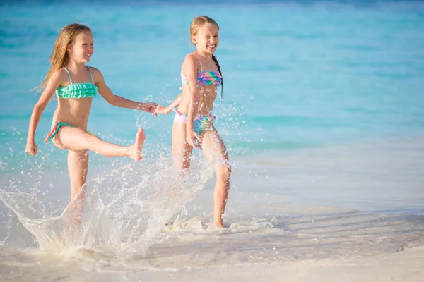 Zwei kleine glückliche Mädchen haben viel Spaß am tropischen Strand und spielen zusammen im flachen Wasser. — Stockfoto