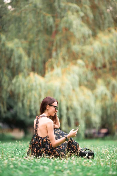 一个可爱的女人坐在公园里，一边看手机上的短信. — 图库照片