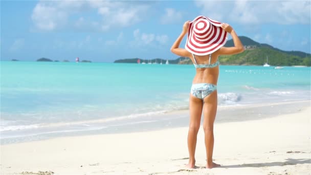 Чарівна маленька дівчинка у великому капелюсі, що йде уздовж пляжу з білим піском — стокове відео