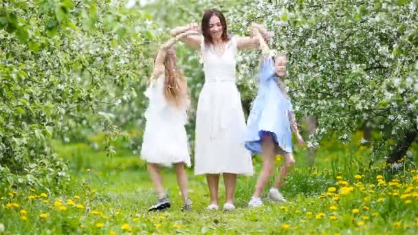 Очаровательные маленькие девочки с молодой матерью в цветущем саду в прекрасный весенний день веселятся вместе — стоковое видео