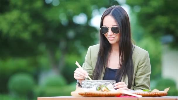 Mujer joven comiendo fideos para llevar en la calle — Vídeo de stock