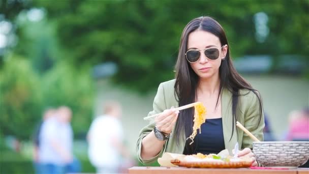 Mujer joven comiendo fideos para llevar en la calle — Vídeos de Stock